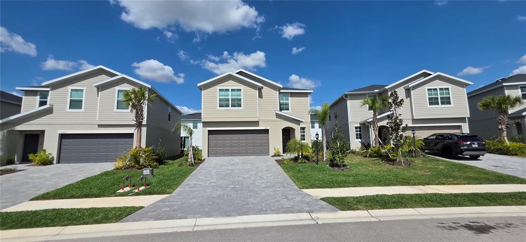 Three two-story suburban houses with paved driveways and garages stand under a blue sky — 13851 LILAC SKY TERRACE UNIT NA, BRADENTON, FL