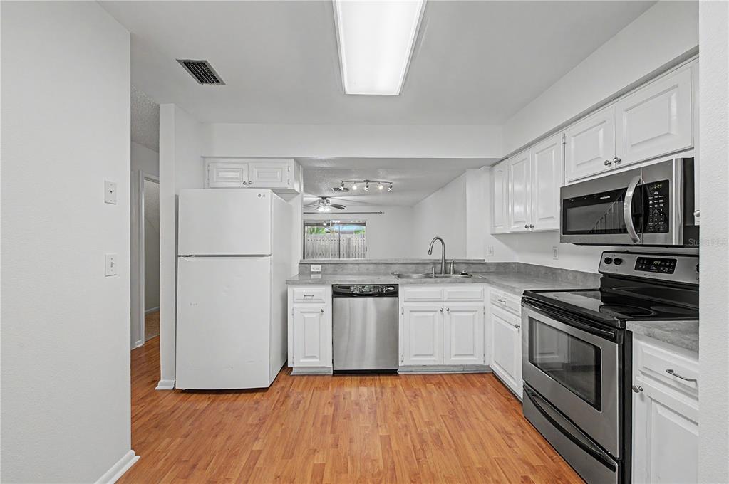 A kitchen with white cabinets, stainless steel appliances, and wood-look flooring — 13856 STONE MILL WAY, TAMPA, FL