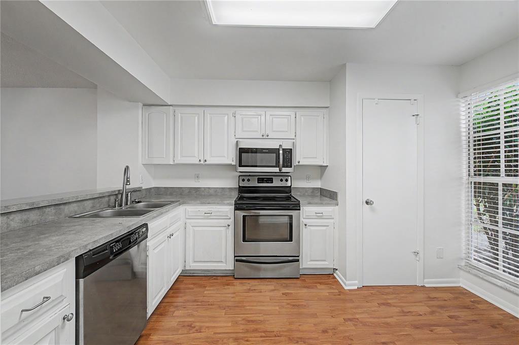 A kitchen features white cabinets, stainless steel appliances, gray countertops, and wood-look flooring — 13856 STONE MILL WAY, TAMPA, FL