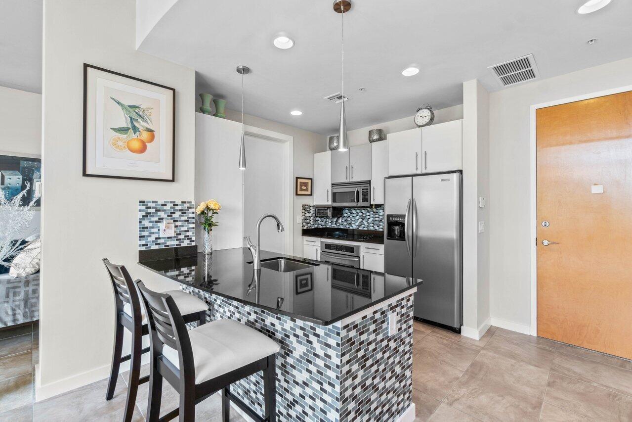 A modern kitchen features a black granite island, stainless steel appliances, and mosaic tile accents — 335 SE 6th Avenue # 304, Delray Beach FL 33483, DELRAY BEACH, FL