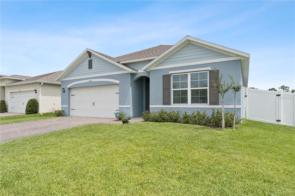 A single-story blue house features a two-car garage, a front lawn, and white fencing — 5825 ARBORETUM STREET, ST CLOUD, FL