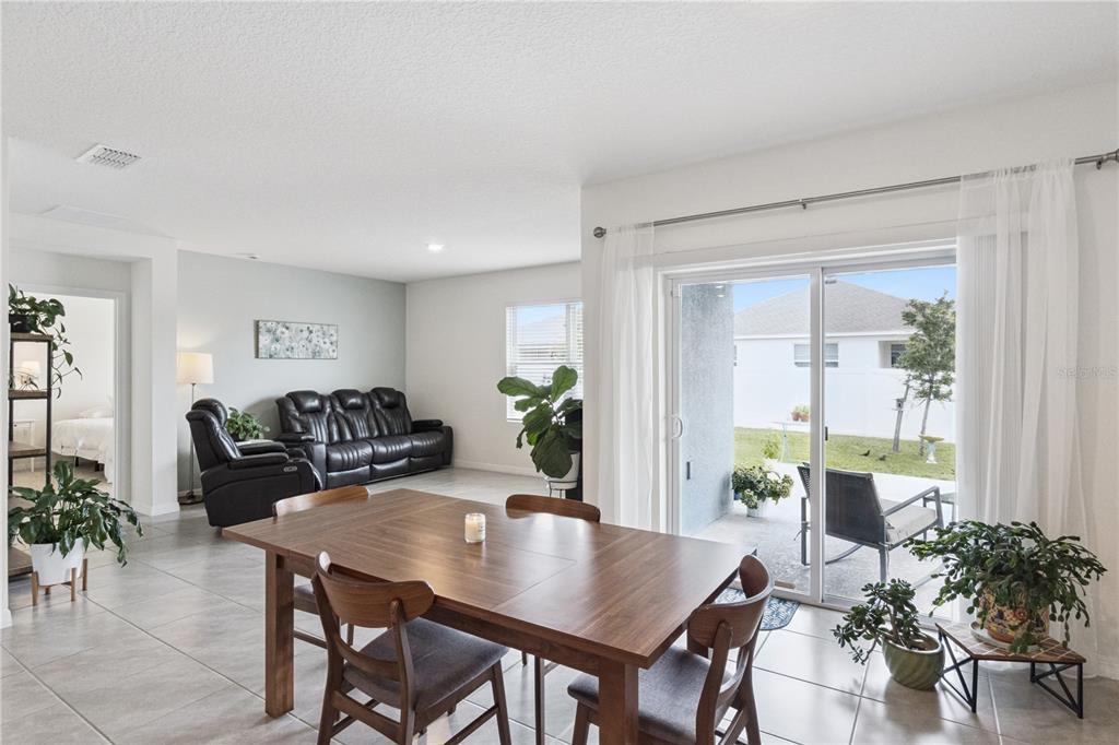 A dining area with a wooden table opens to a living room and a patio — 5825 ARBORETUM STREET, ST CLOUD, FL