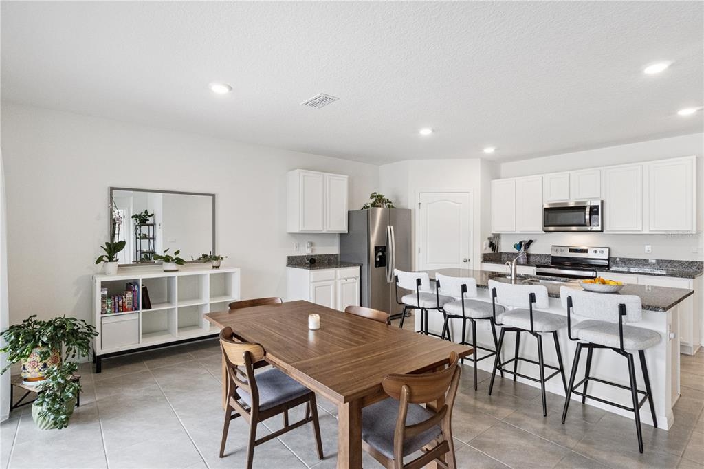 A kitchen with white cabinets and granite countertops opens to a dining area with tile flooring — 5825 ARBORETUM STREET, ST CLOUD, FL