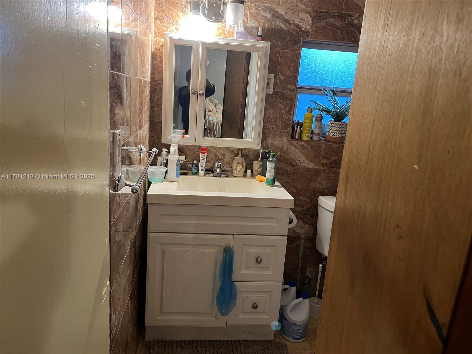 A bathroom features a white vanity, a medicine cabinet, and brown marble-style wall tiles — 6546 SW 20th Ct, Miramar FL 33023, MIRAMAR, FL