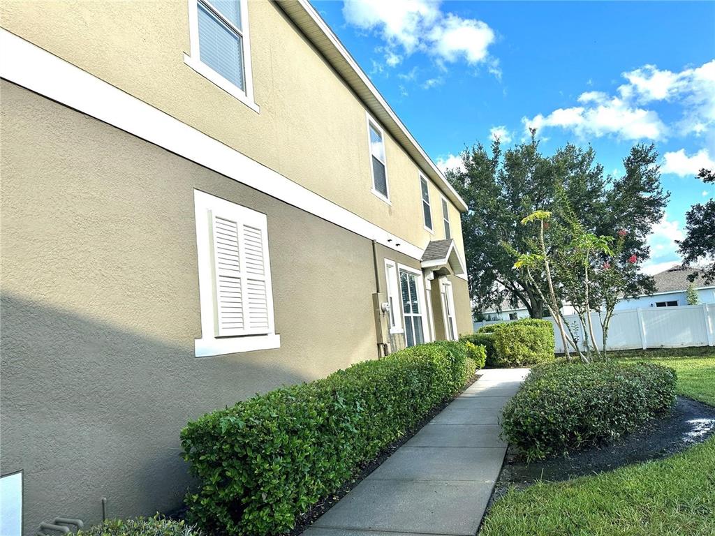 A side view of a tan two-story house with a sidewalk and manicured hedges — 1971 ESTANCIA CIRCLE, KISSIMMEE, FL