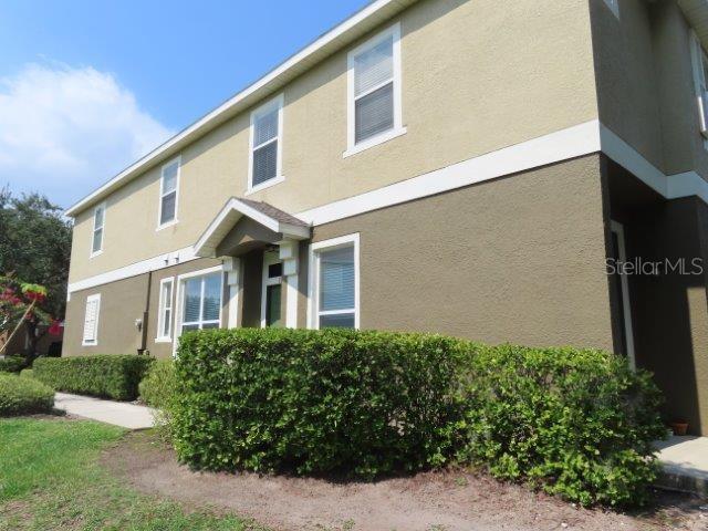 A two-story building exterior with tan and brown stucco walls and a green hedge — 1971 ESTANCIA CIRCLE, KISSIMMEE, FL
