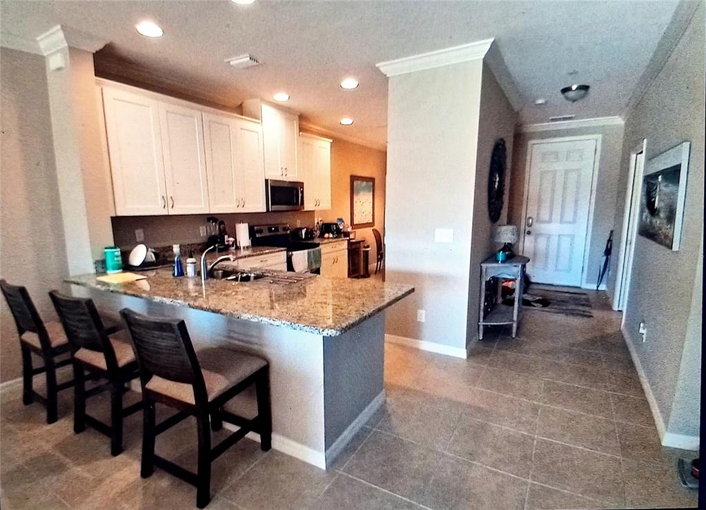 A kitchen with granite countertops, white cabinets, and a breakfast bar with three stools — 12740 SORRENTO WAY UNIT 101, BRADENTON, FL