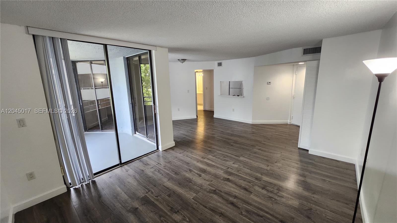 An empty living area features dark wood-look flooring, white walls, and a sliding glass door — 8305 SW 152nd Ave # 404, Miami FL 33193, MIAMI, FL