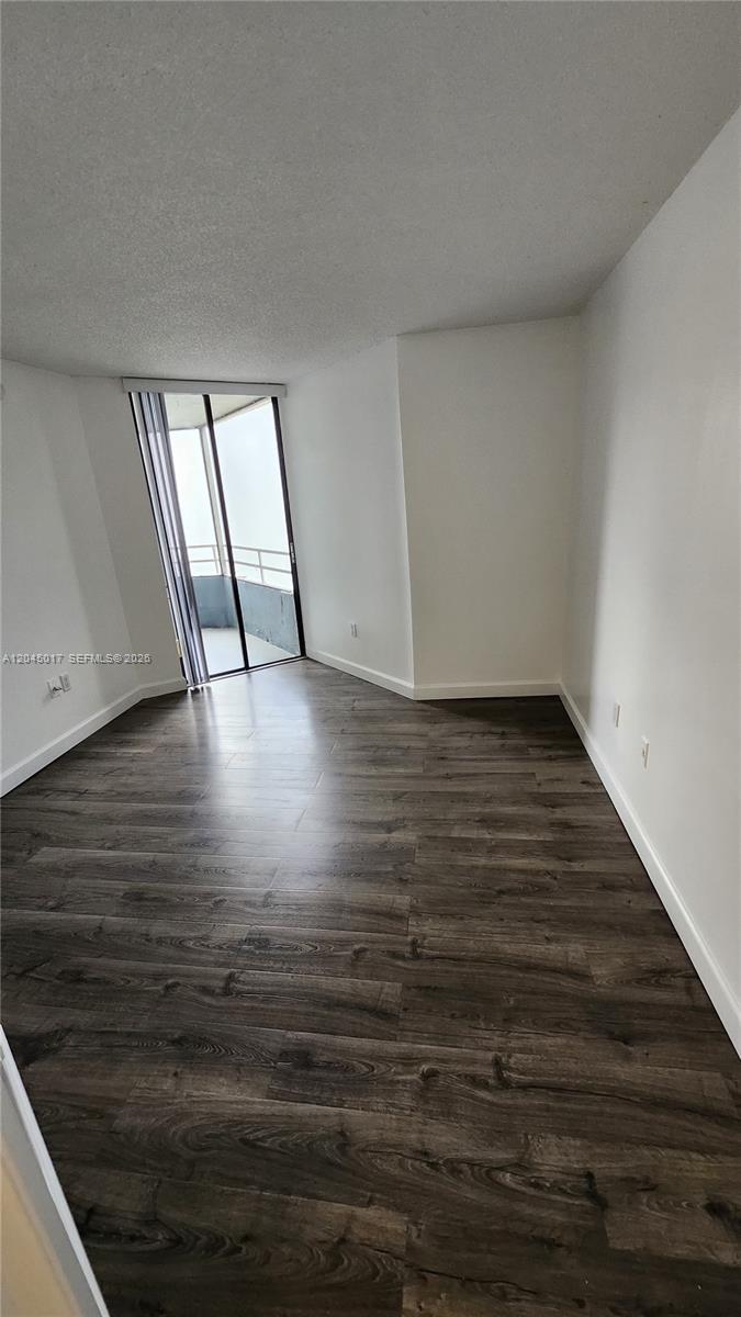 An empty room features dark wood-look flooring, white walls, and a sliding glass door — 8305 SW 152nd Ave # 404, Miami FL 33193, MIAMI, FL