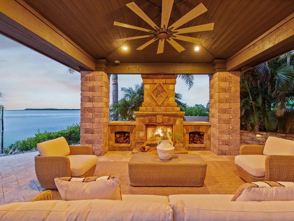 A covered outdoor patio features a stone fireplace, wicker furniture, and a view of water — 2057 N POINTE ALEXIS DRIVE, TARPON SPRINGS, FL