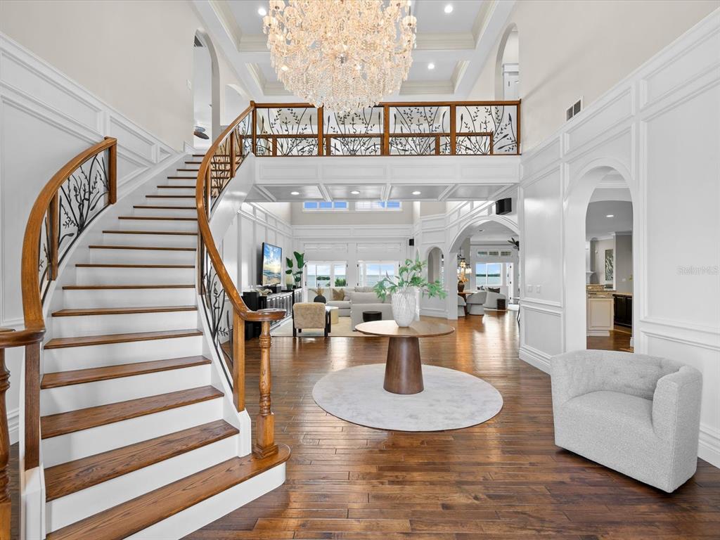 A grand foyer features a curved wooden staircase, a large crystal chandelier, and hardwood floors — 2057 N POINTE ALEXIS DRIVE, TARPON SPRINGS, FL