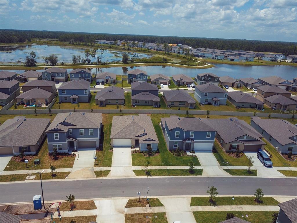 An aerial view shows a suburban neighborhood with houses, a pond, and a forest — 22430 BLAZING STAR, LAND O LAKES, FL