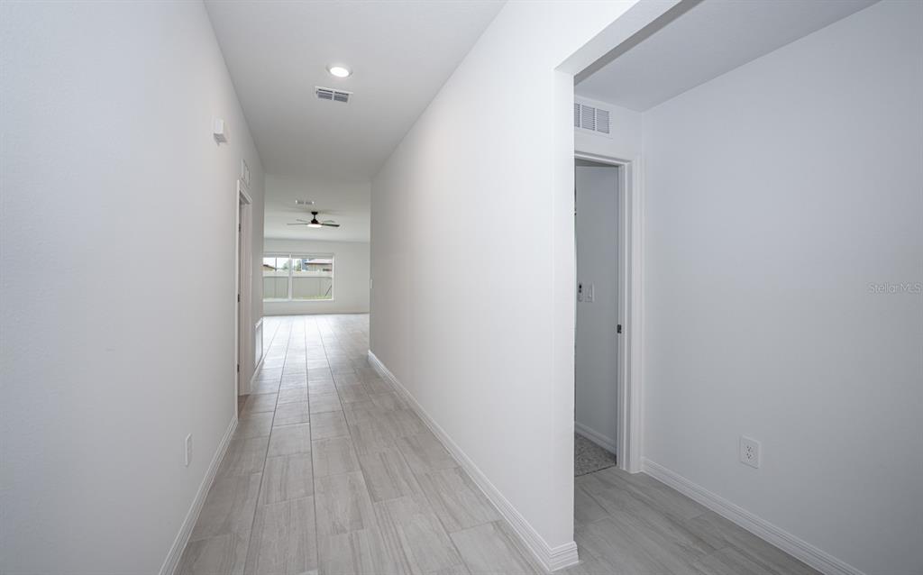A hallway with light-colored tile flooring leads toward a bright room with a ceiling fan — 22430 BLAZING STAR, LAND O LAKES, FL