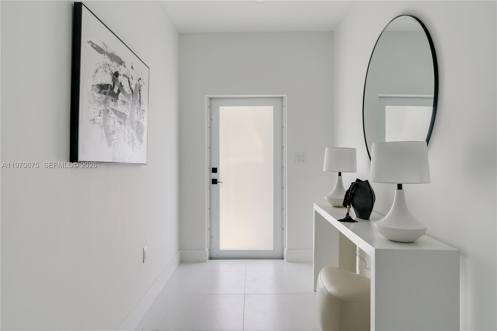 A minimalist entryway features white walls, tile flooring, a console table, and a round mirror — 4789 NW 1st St, Miami FL 33126, MIAMI, FL