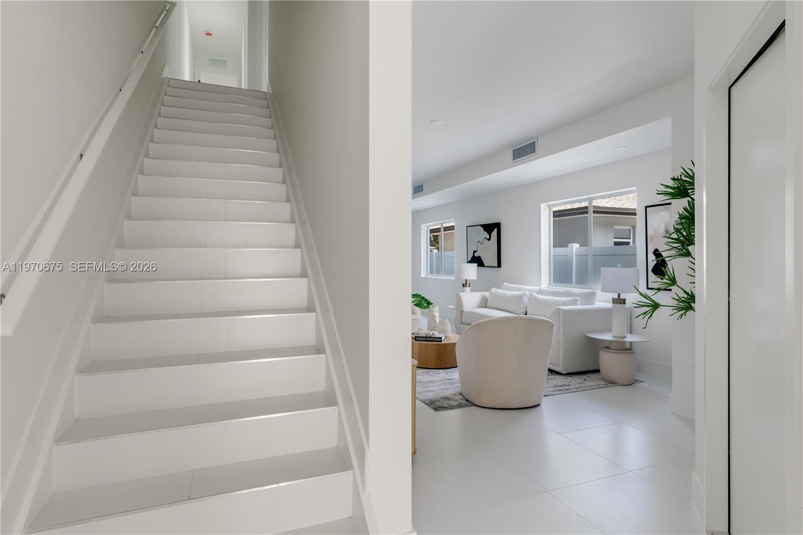 A white staircase leads upward next to a bright living room with tile flooring — 4789 NW 1st St, Miami FL 33126, MIAMI, FL