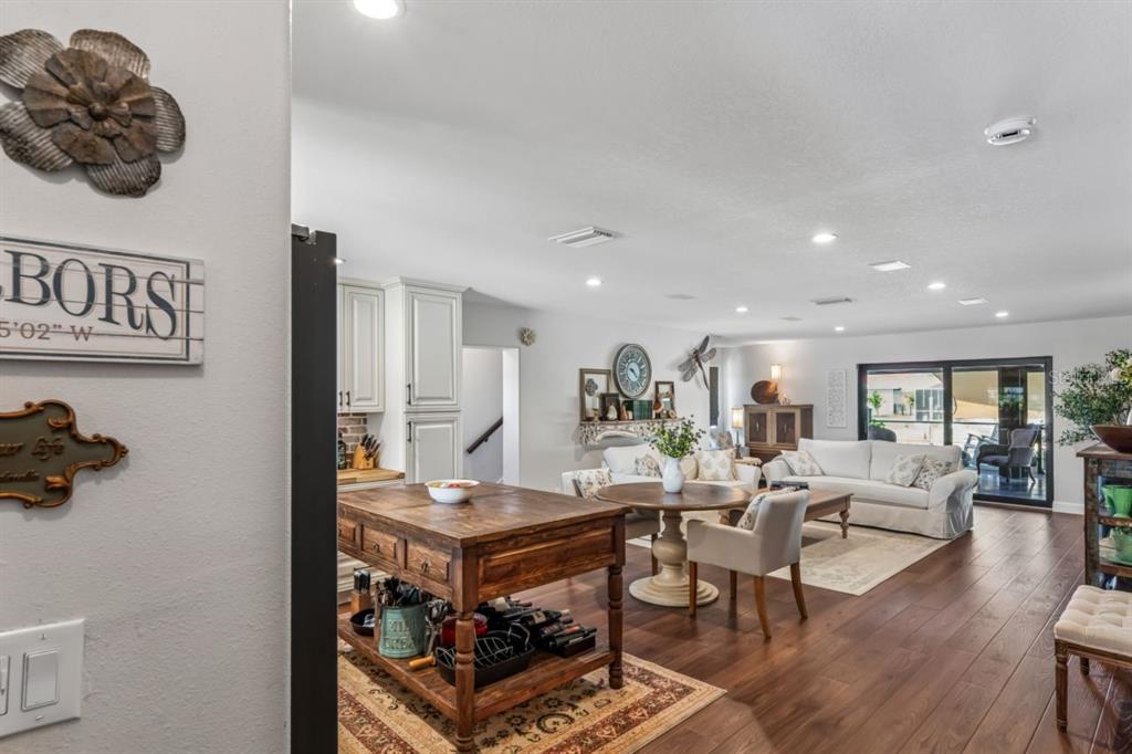 An open-concept living area features a kitchen island, dining table, and white sofa on wood floors — 4903 BLUE HERON DRIVE, NEW PORT RICHEY, FL