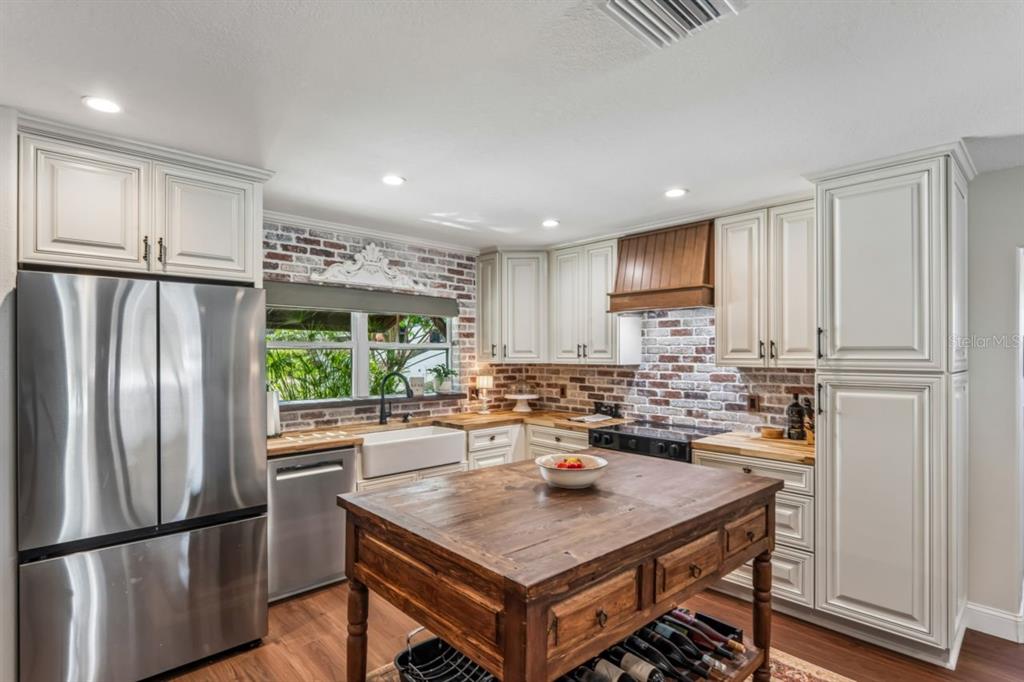 A kitchen features white cabinetry, a wooden island, stainless steel appliances, and a brick backsplash — 4903 BLUE HERON DRIVE, NEW PORT RICHEY, FL