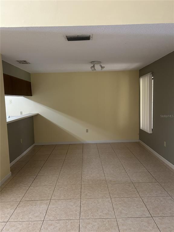 An interior view of a room with light-colored tile flooring, yellow walls, and a breakfast bar — 484 PRESTWICK PLACE, KISSIMMEE, FL