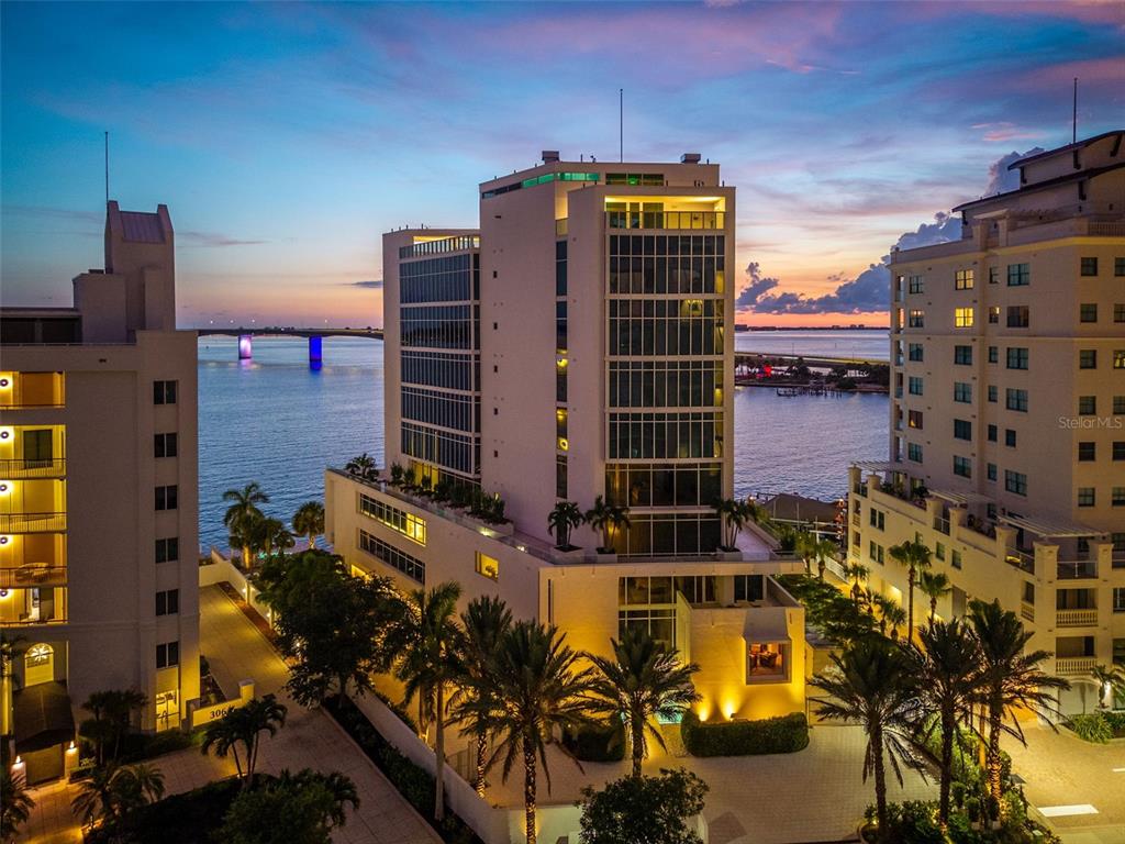 An aerial view of a modern high-rise building at sunset near a bridge and water — 280 GOLDEN GATE POINT UNIT 300, SARASOTA, FL