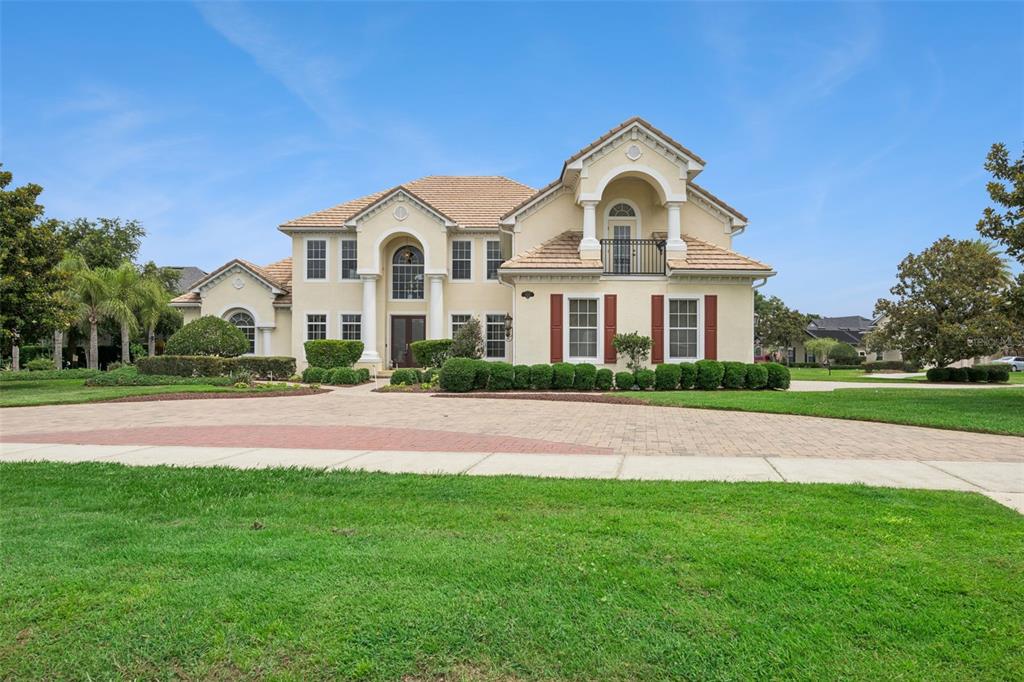 A large, two-story beige house with a tiled roof and a circular paved driveway — 1692 ORANGE THORPE LANE, CLERMONT, FL