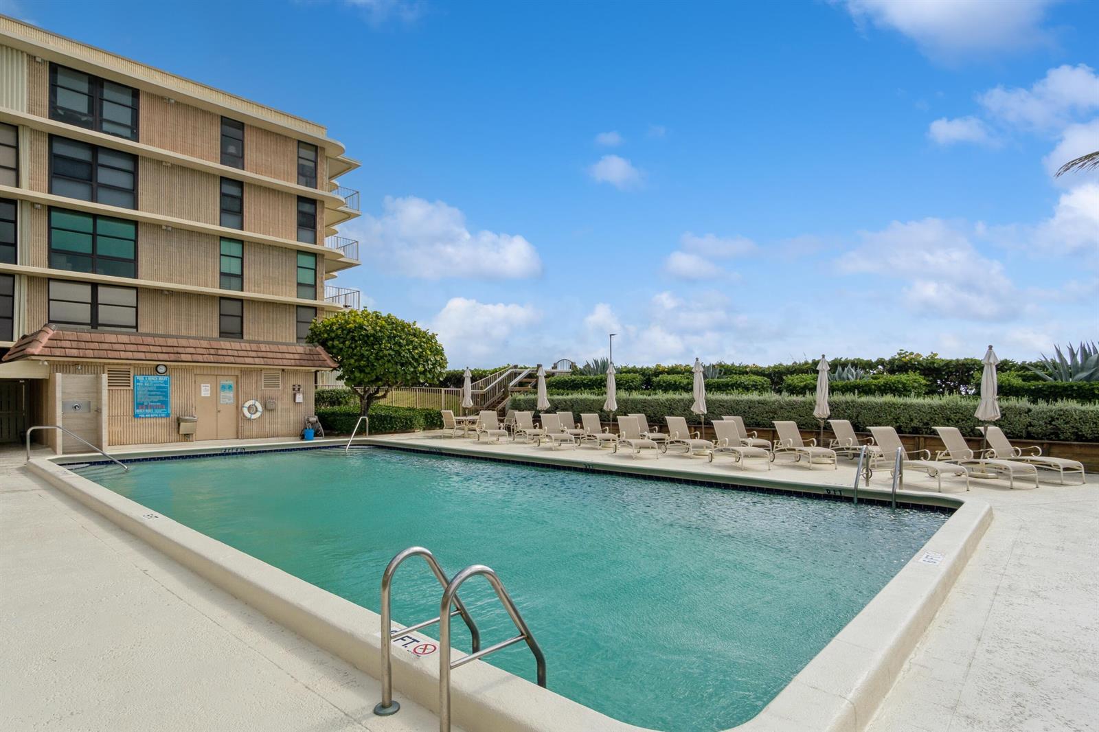 A rectangular swimming pool sits beside a multi-story building with lounge chairs on the deck — 3200 S Ocean Boulevard # B104, Palm Beach FL 33480, PALM BEACH, FL