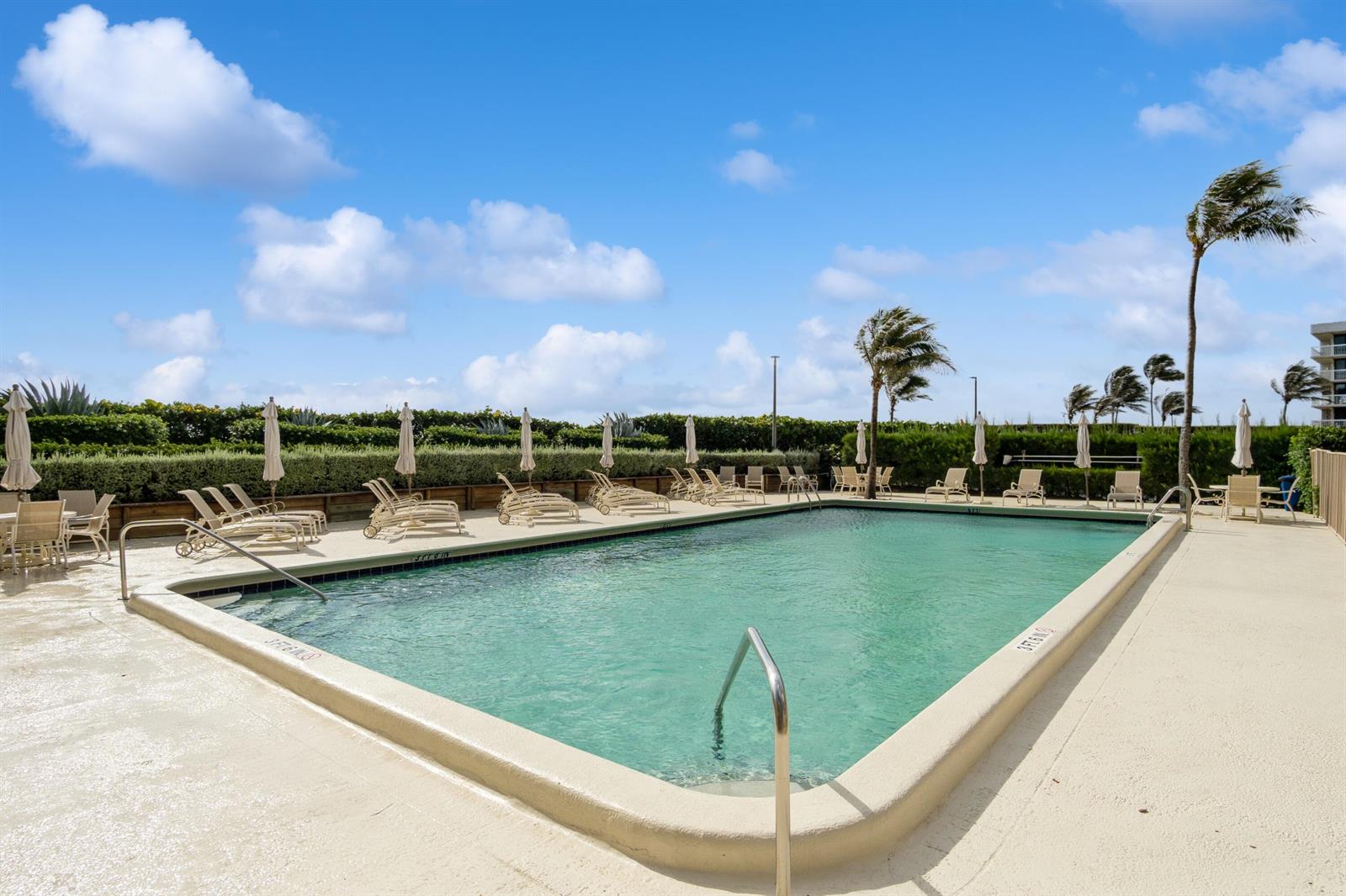 An outdoor swimming pool surrounded by lounge chairs, umbrellas, and palm trees under a blue sky — 3200 S Ocean Boulevard # B104, Palm Beach FL 33480, PALM BEACH, FL