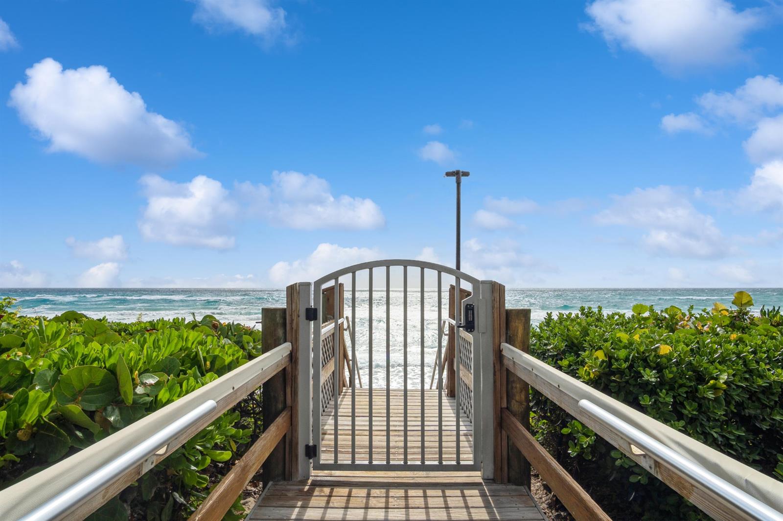 A wooden walkway with a metal gate leads toward the ocean through green foliage — 3200 S Ocean Boulevard # B104, Palm Beach FL 33480, PALM BEACH, FL