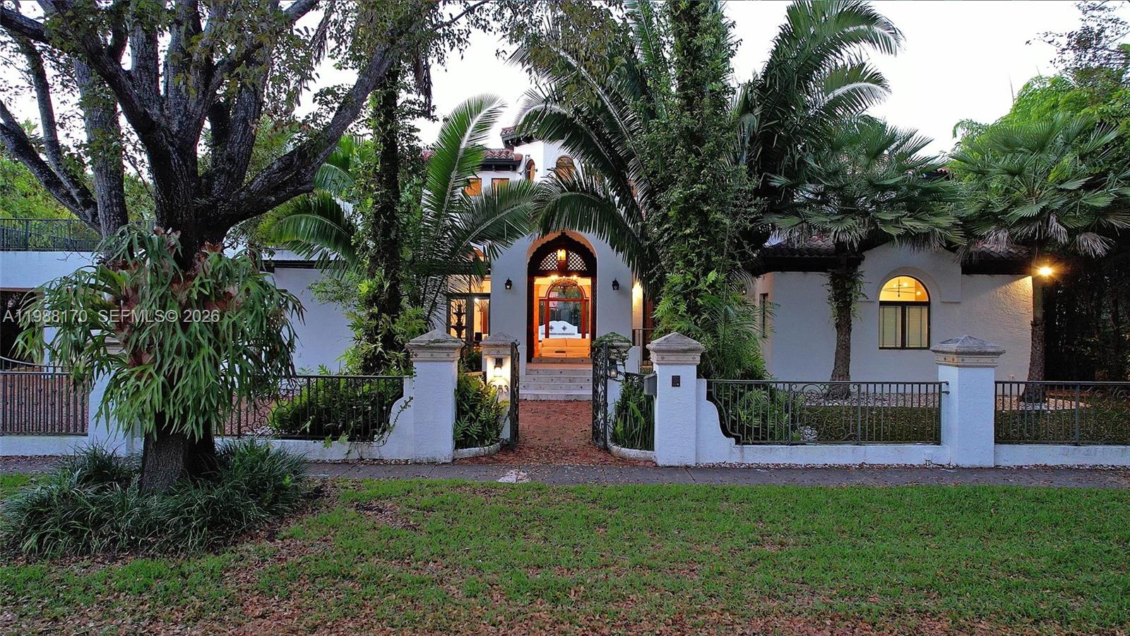 A white house with a gated entrance and palm trees is viewed from the street — 1253 Sorolla Ave, Coral Gables FL 33134, CORAL GABLES, FL