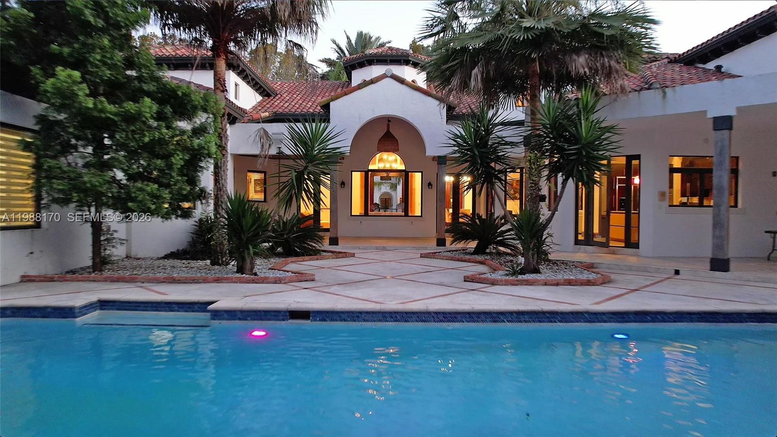 A swimming pool sits in front of a white Mediterranean-style house with a tiled roof — 1253 Sorolla Ave, Coral Gables FL 33134, CORAL GABLES, FL
