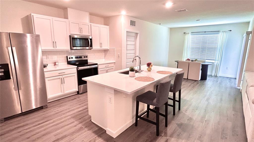 A modern kitchen features white cabinets, stainless steel appliances, and a central island with seating — 3919 MALAWI TRAIL, ST CLOUD, FL