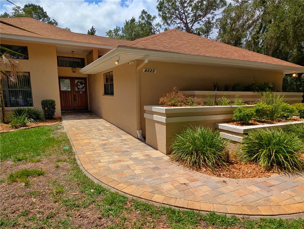 A paved walkway leads to the front entrance of a tan house with a roof — 4023 N RINGWOOD CIRCLE, HERNANDO, FL