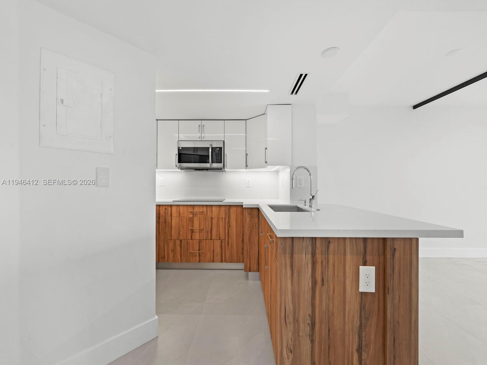 A modern kitchen features white upper cabinets, wood-grain lower cabinets, and a white countertop island — 8215 SW 152nd Ave # 308, Miami FL 33193, MIAMI, FL