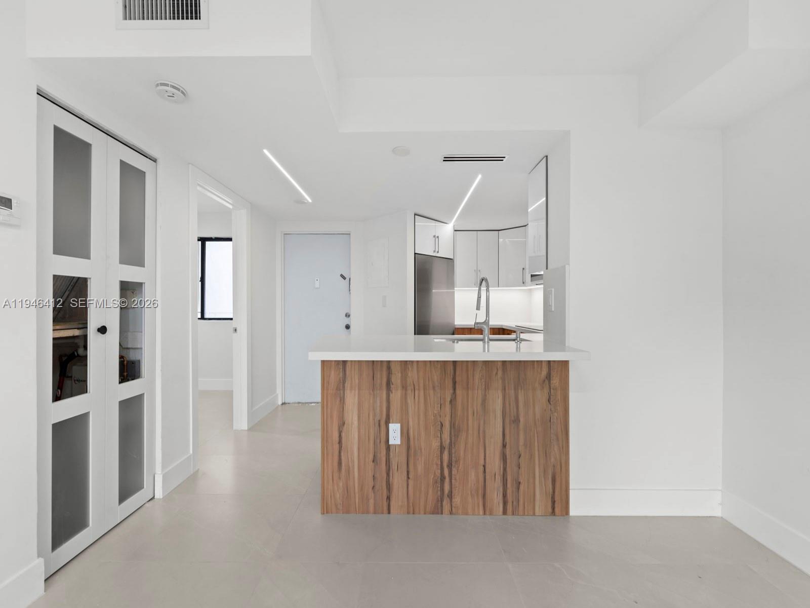 A modern kitchen features white cabinetry, a wood-paneled island, and light-colored tile flooring — 8215 SW 152nd Ave # 308, Miami FL 33193, MIAMI, FL