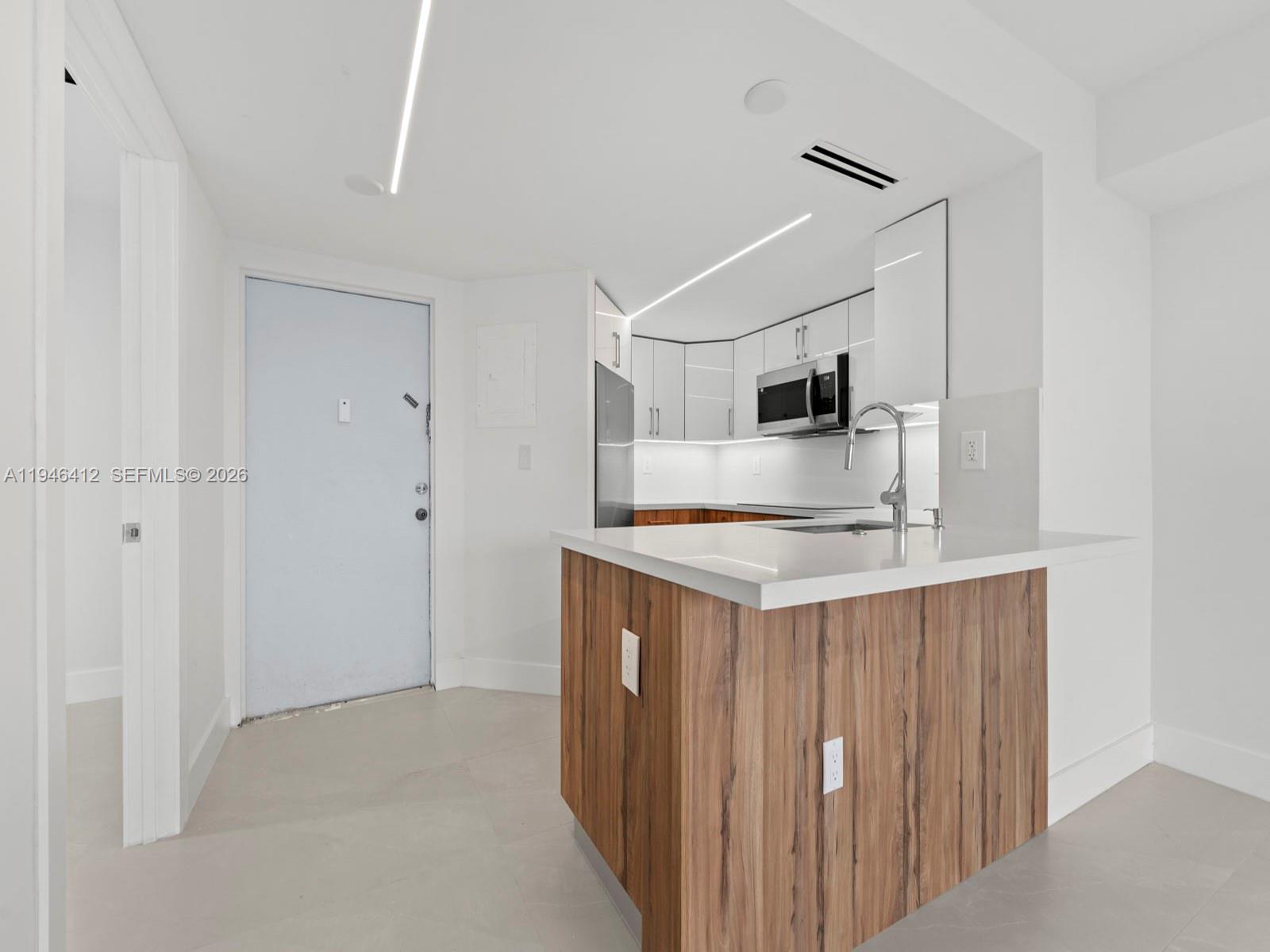 A modern kitchen features white cabinets, wood-paneled island cabinetry, and a white quartz countertop — 8215 SW 152nd Ave # 308, Miami FL 33193, MIAMI, FL