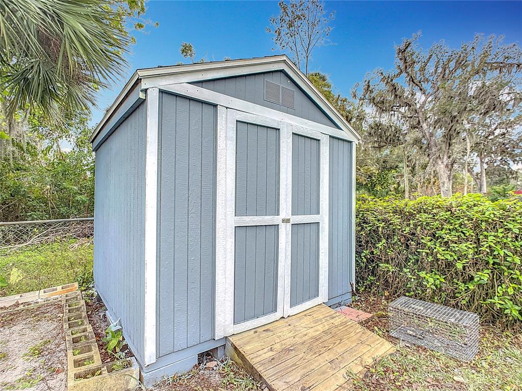 A blue wooden storage shed with white trim and a wooden ramp stands outdoors — 608 POWERS AVENUE, PORT ORANGE, FL