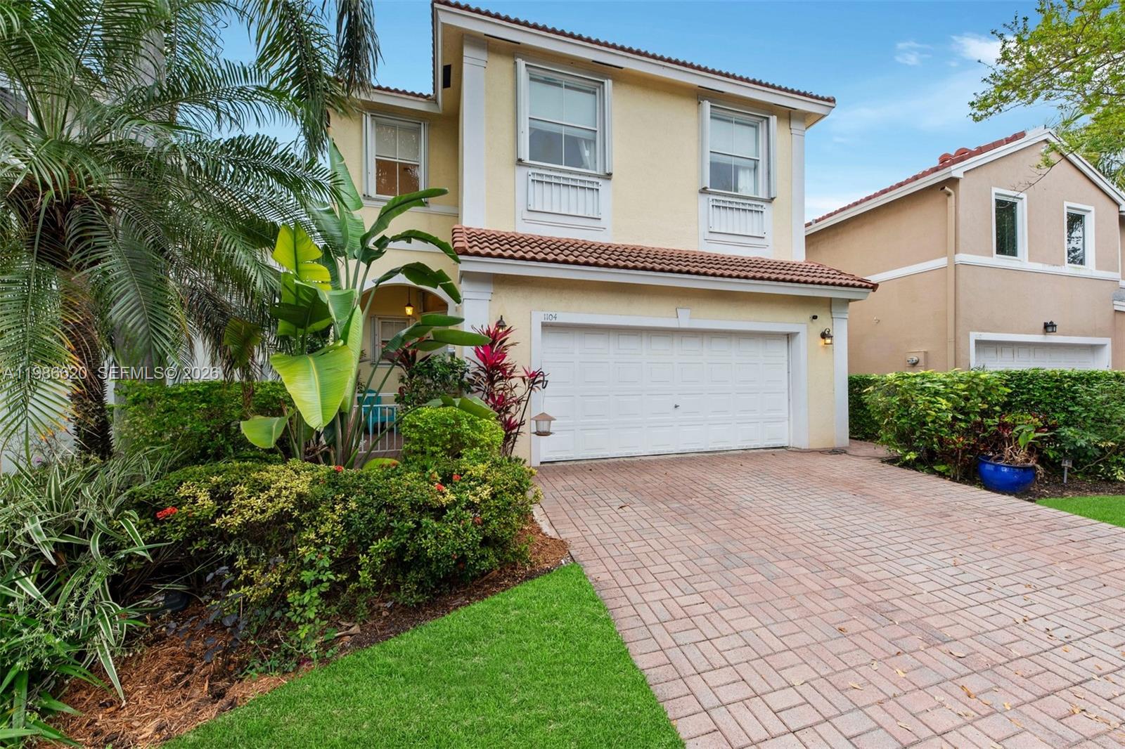 A two-story yellow house with a white garage door and a brick paver driveway — 1104 Redwood St, Hollywood FL 33019, HOLLYWOOD, FL