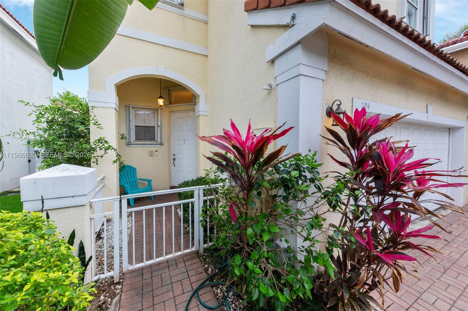 The exterior of a house features a gated entryway, a white door, and tropical plants — 1104 Redwood St, Hollywood FL 33019, HOLLYWOOD, FL
