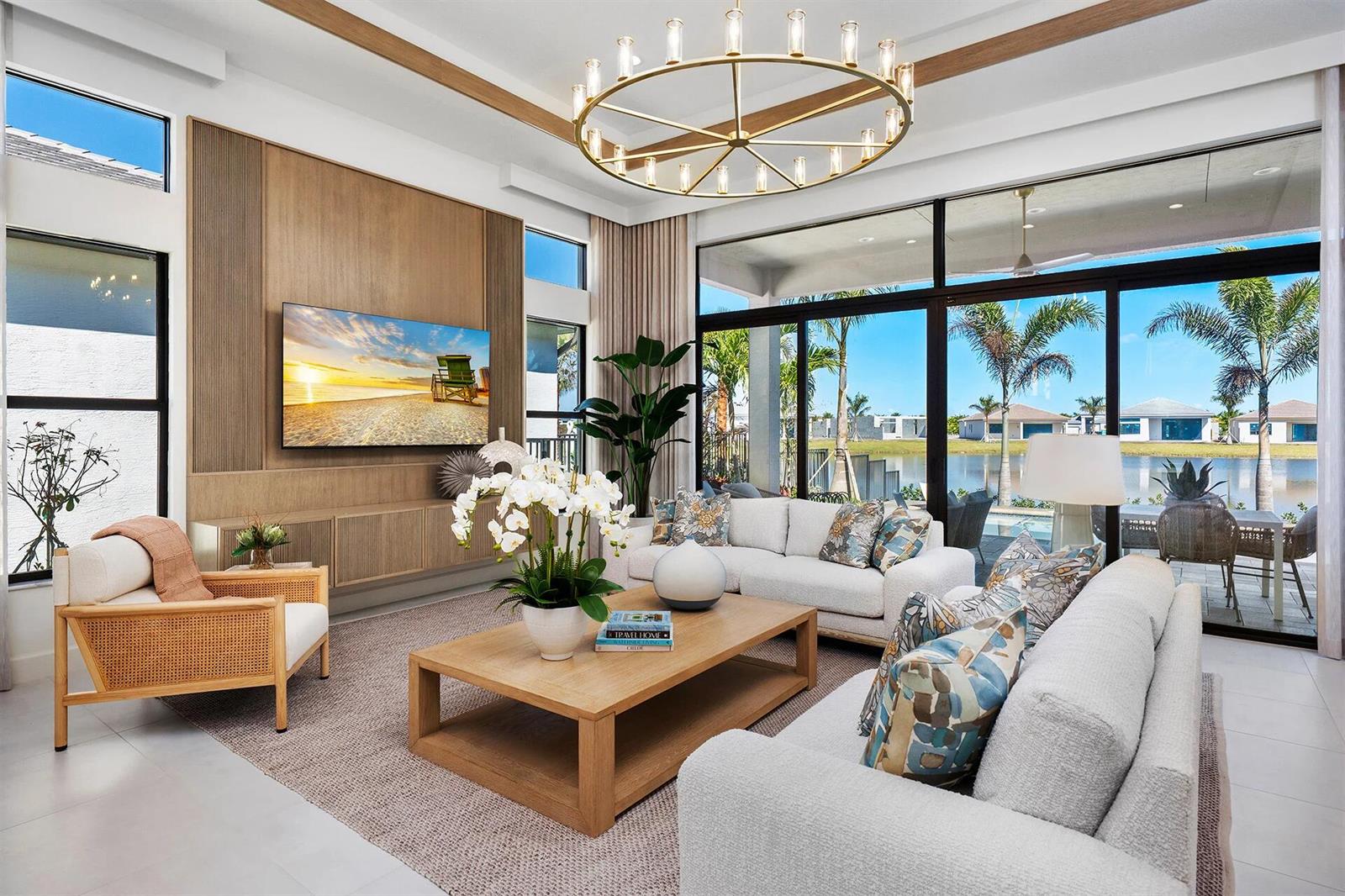 A modern living room features wood paneling, a large chandelier, and floor-to-ceiling windows overlooking water — 9124 Red Robin Lane, Boynton Beach FL 33473, BOYNTON BEACH, FL