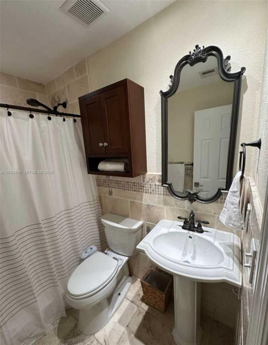 A bathroom features a pedestal sink, a toilet, a shower curtain, and a wall-mounted cabinet — MIAMI, FL