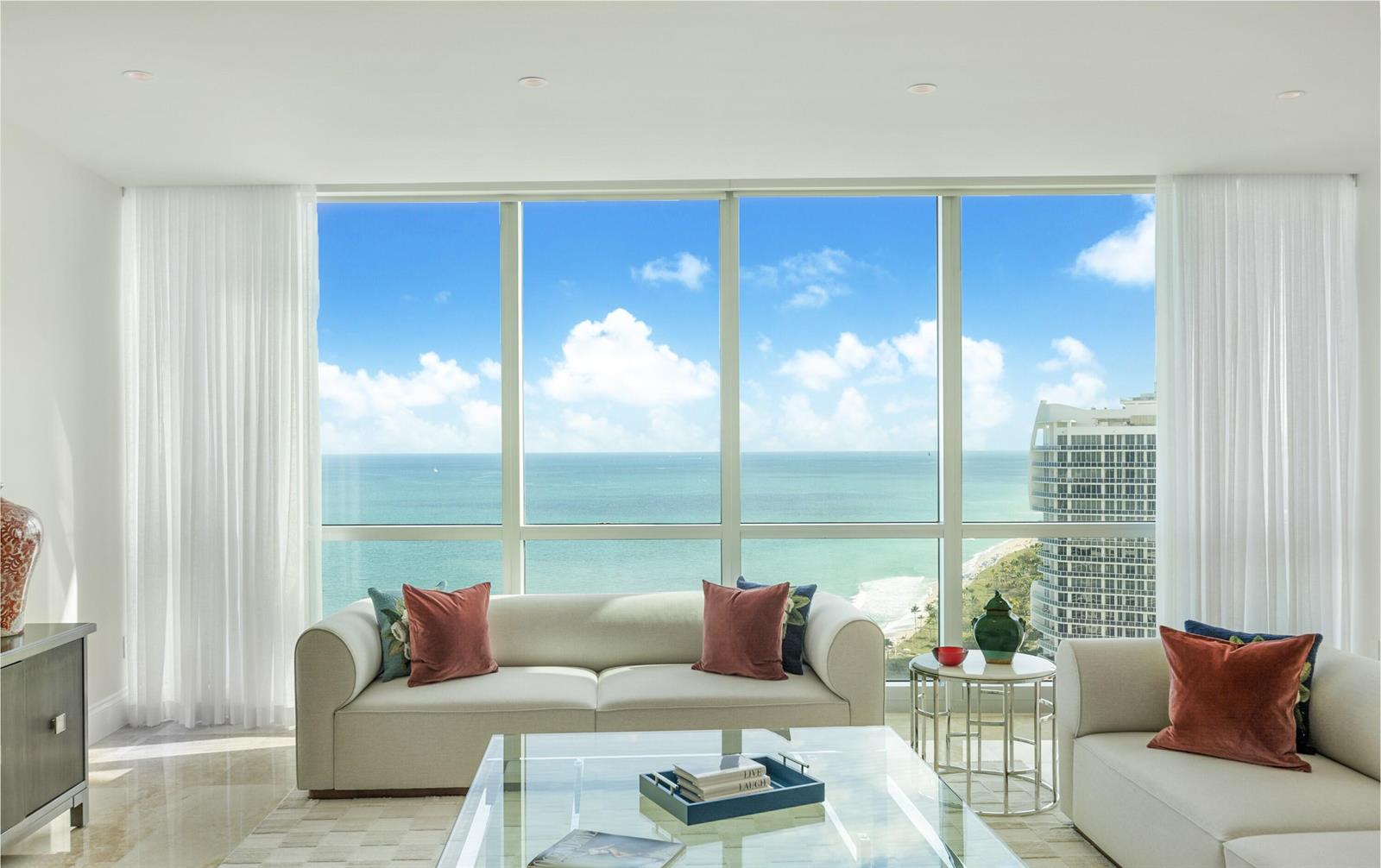 A living room with light sofas faces floor-to-ceiling windows overlooking the ocean and city — 10295 Collins Avenue # 2203, Bal Harbour FL 33154, BAL HARBOUR, FL