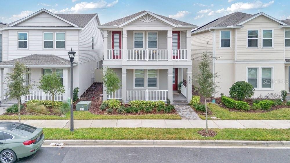 A two-story house with a front porch and balcony sits between two neighboring homes — 15026 SUMMER HARVEST STREET, WINTER GARDEN, FL