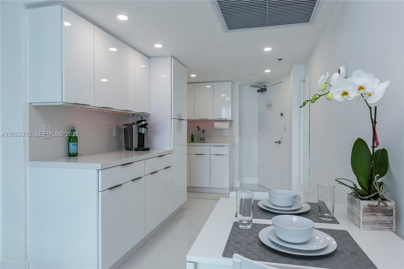 A modern white kitchen features glossy cabinets, quartz countertops, and a small dining table — 5445 Collins Ave # 1232, Miami Beach FL 33140, MIAMI BEACH, FL