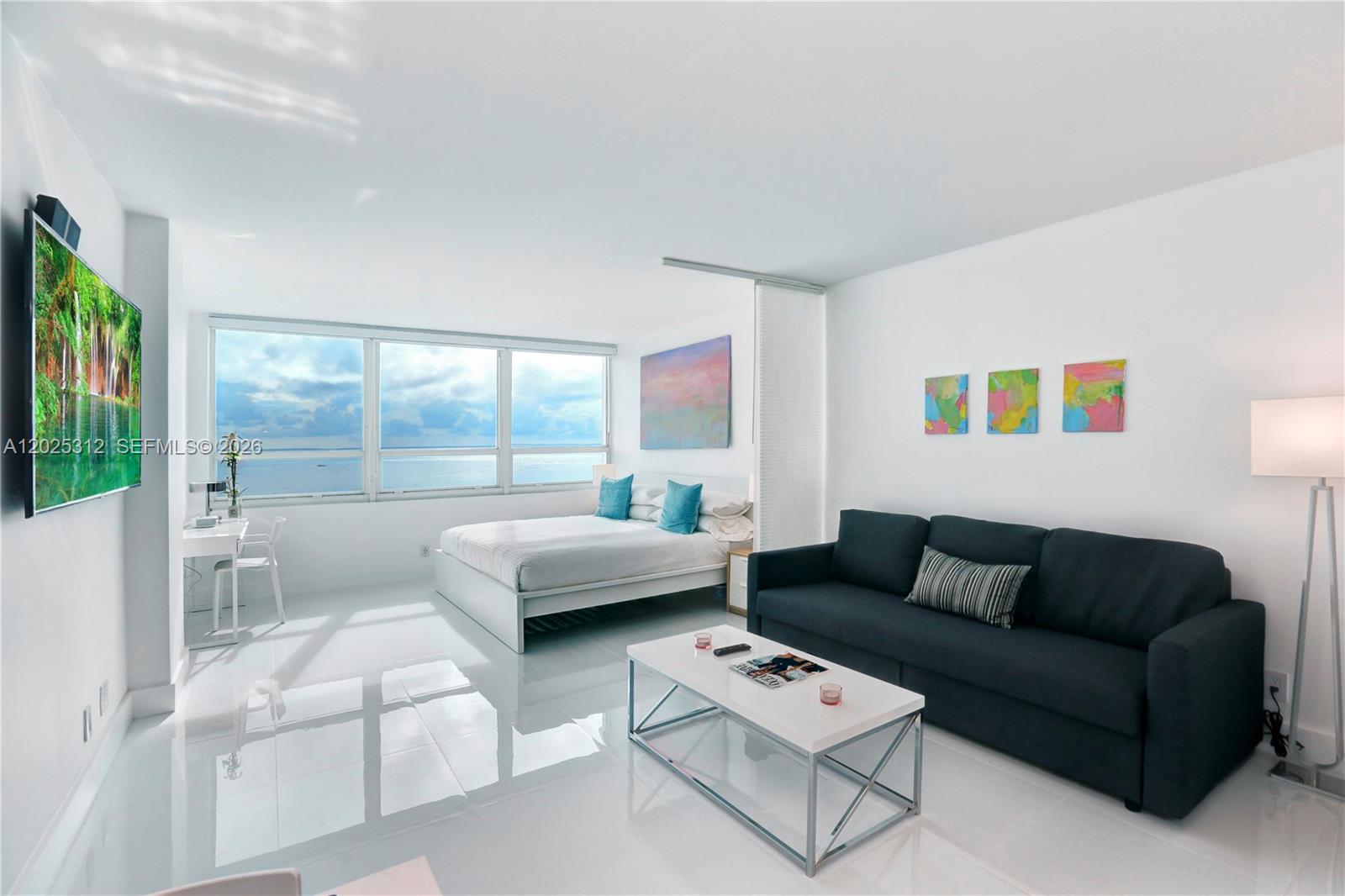 A studio apartment features a bed, dark sofa, white coffee table, and ocean views — 5445 Collins Ave # 1232, Miami Beach FL 33140, MIAMI BEACH, FL