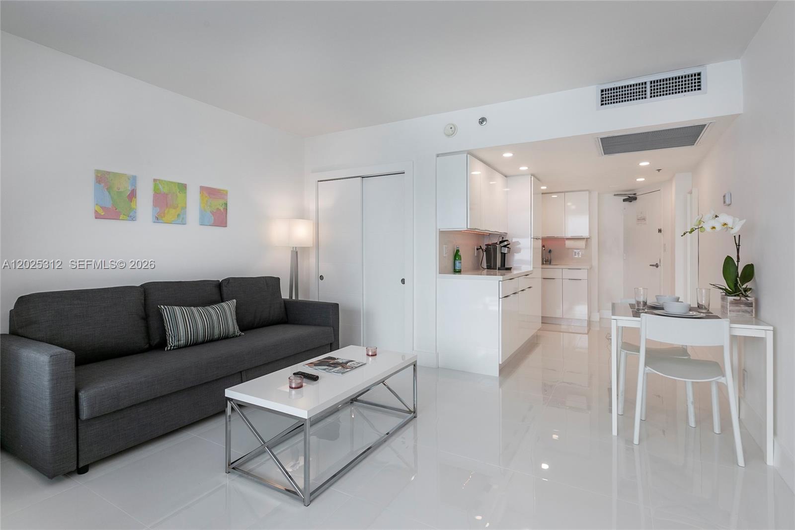 A modern living room features a grey sofa, white coffee table, and an adjacent kitchen — 5445 Collins Ave # 1232, Miami Beach FL 33140, MIAMI BEACH, FL