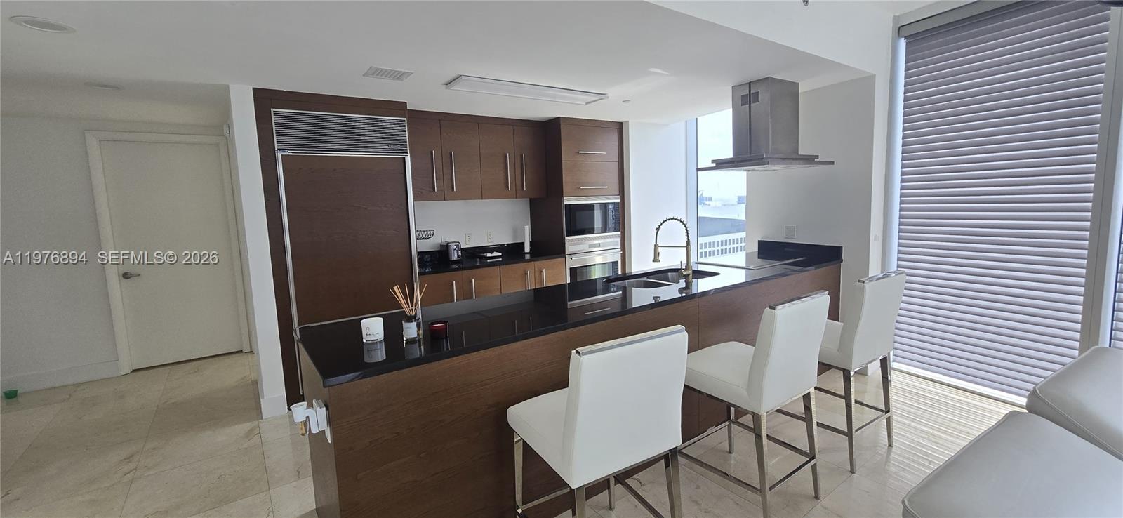 A modern kitchen features dark wood cabinetry, black countertops, and three white bar stools — 495 Brickell Ave # 5310, Miami FL 33131, MIAMI, FL
