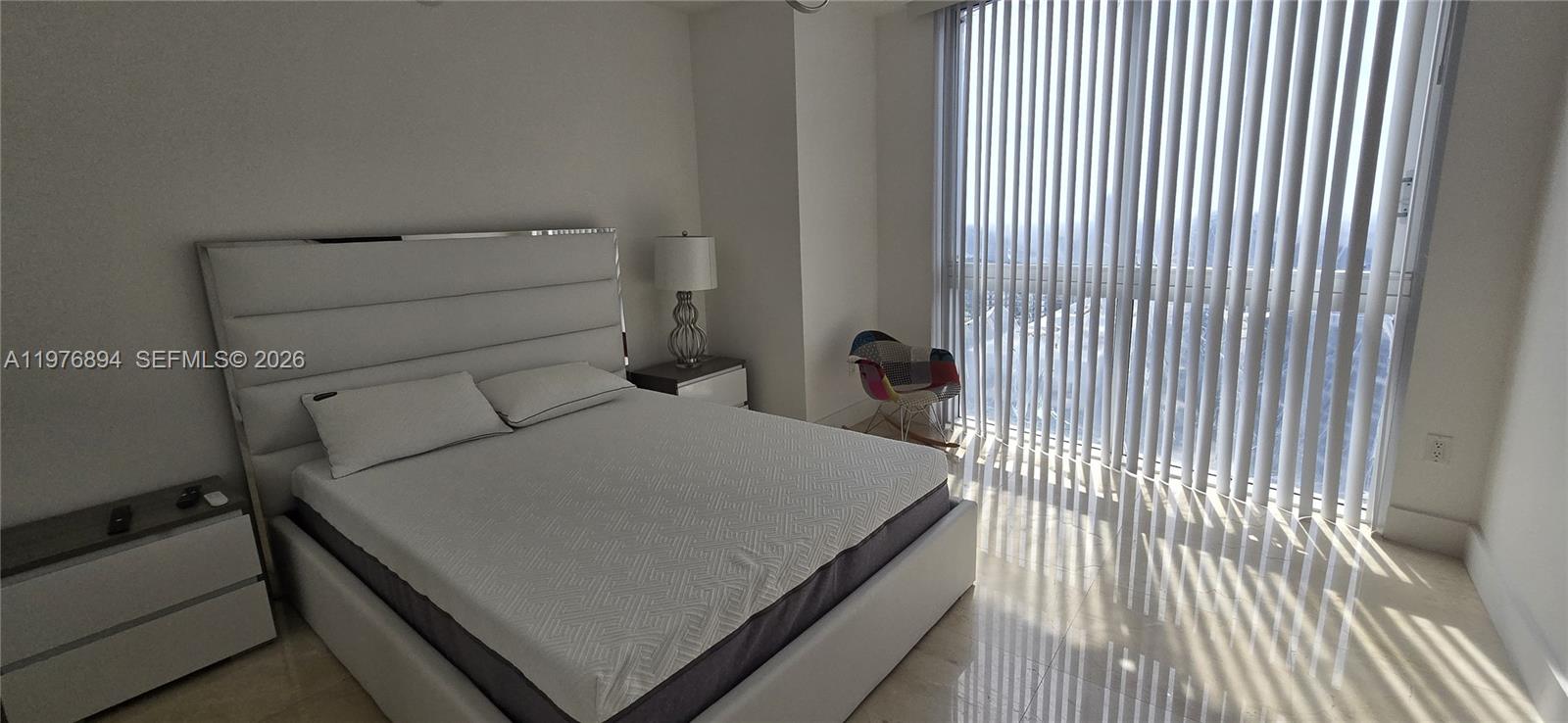 A bedroom features a white upholstered bed, a modern chair, and floor-to-ceiling vertical blinds — 495 Brickell Ave # 5310, Miami FL 33131, MIAMI, FL