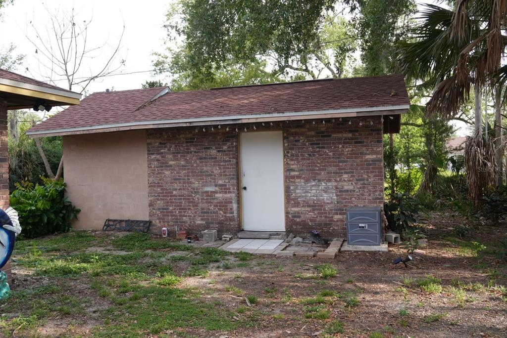 A detached brick shed with a shingled roof and a white door stands outdoors — 1022 LAMPLIGHTER LANE, LAKELAND, FL