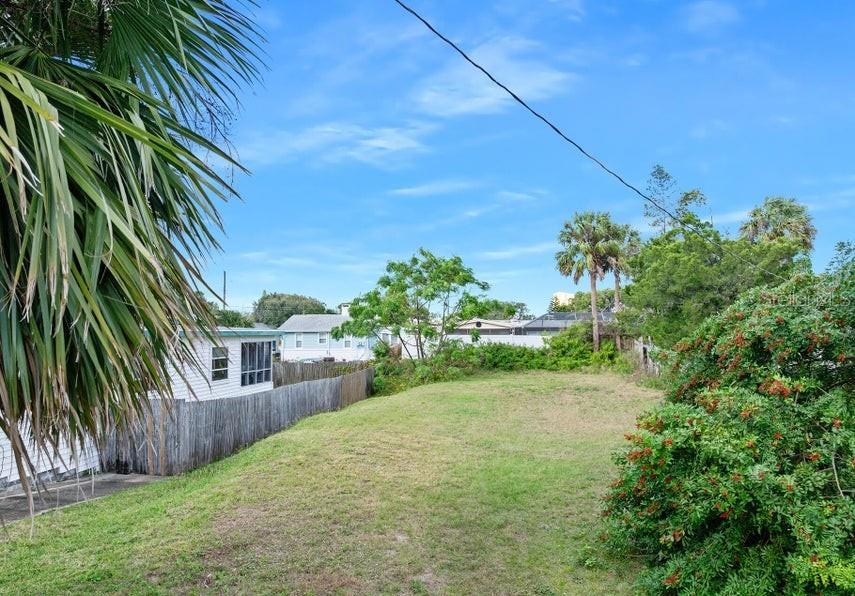 A grassy vacant lot sits next to a white house with a wooden fence — 339 MANHATTAN AVENUE, DAYTONA BEACH, FL