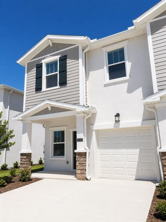 A two-story townhouse with a white stucco facade, stone accents, and a single-car garage — 3115 MINDFULLNESS DRIVE, CLERMONT, FL