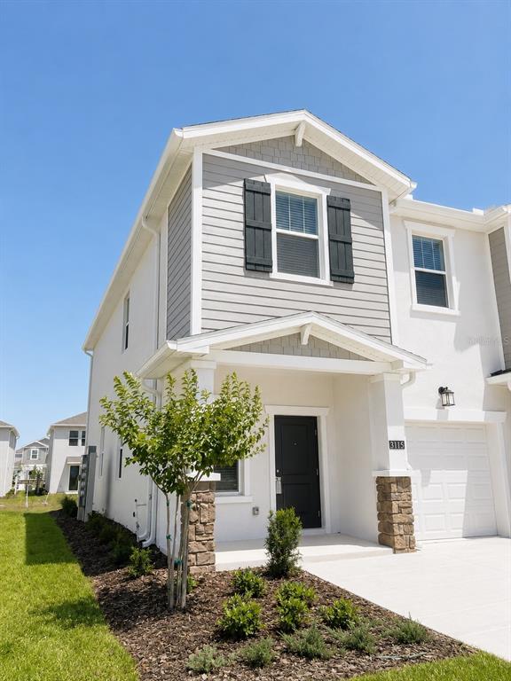 A two-story townhouse exterior features light gray siding, stone accents, and a white garage door — 3115 MINDFULLNESS DRIVE, CLERMONT, FL
